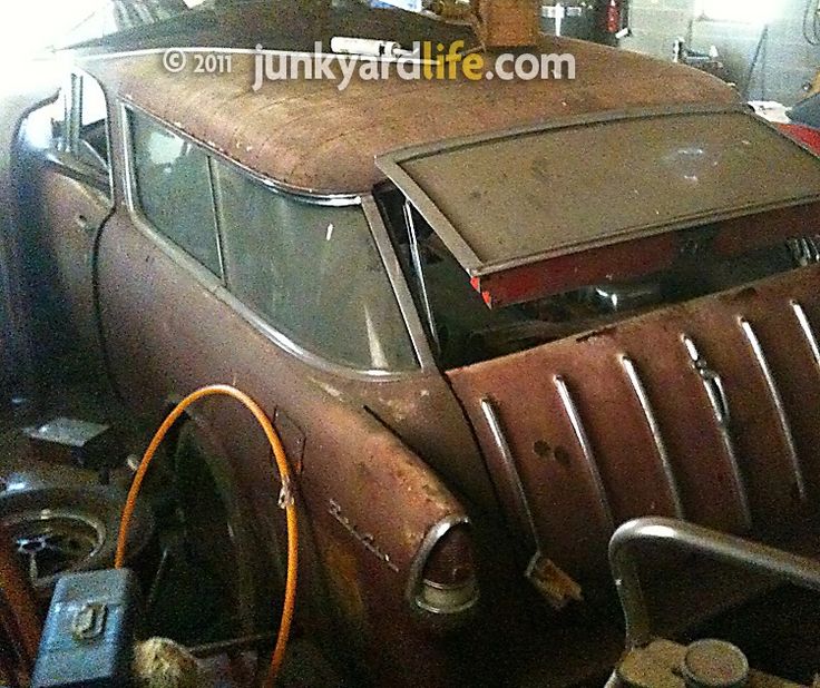 an old rusted out car is parked in a garage with other cars behind it