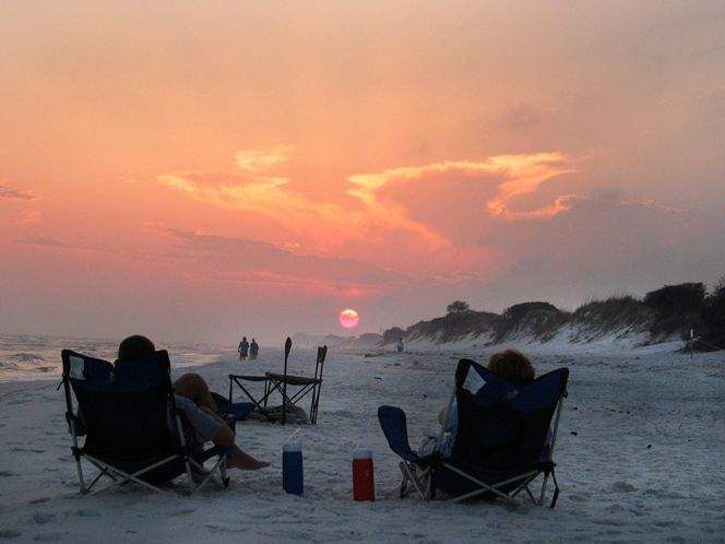 two people are sitting in lawn chairs on the beach watching the sun rise over the ocean