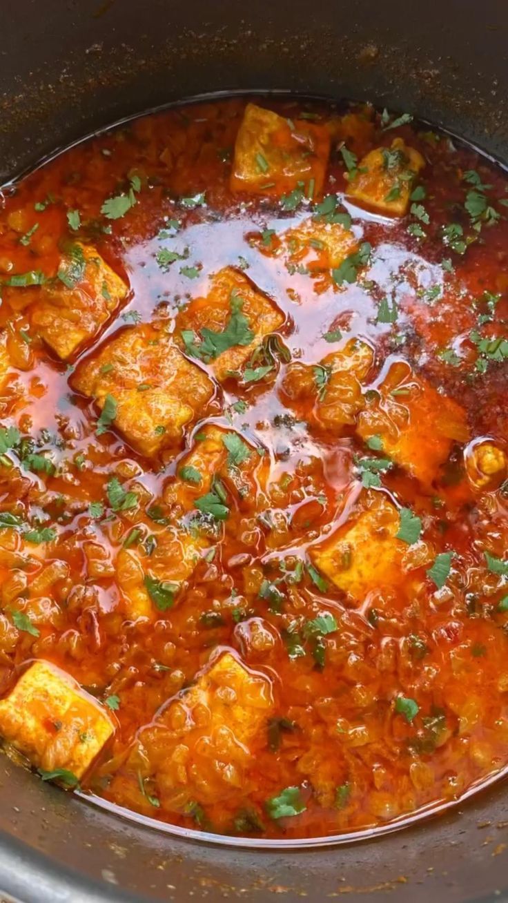 a pot full of stew with tofu cubes and garnish on top