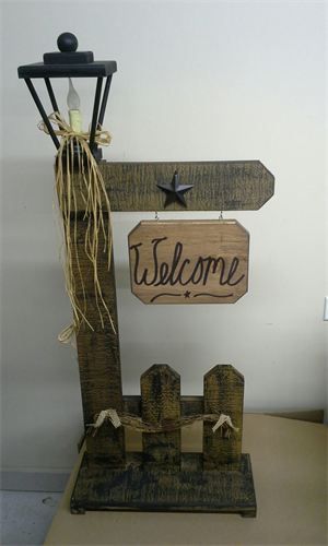 a wooden welcome sign hanging from the side of a wall next to a lamp post