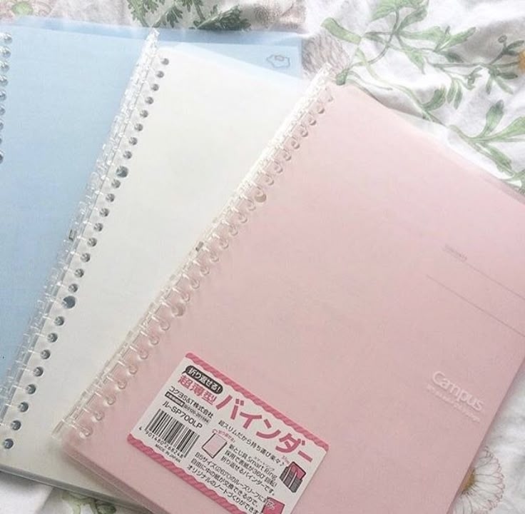 three notebooks sitting next to each other on top of a floral print bed sheet