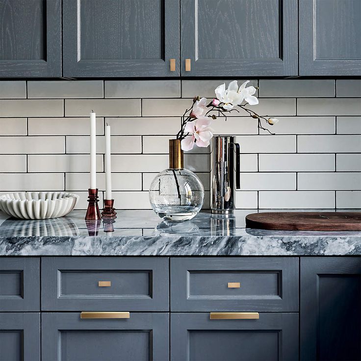 a kitchen with gray cabinets and marble counter tops, gold pulls on the handles to match the cabinetry