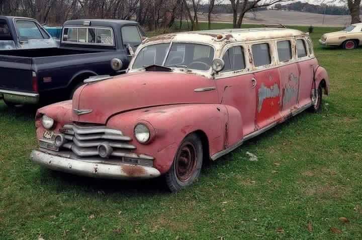 an old red and white van is parked in the grass next to other antique cars