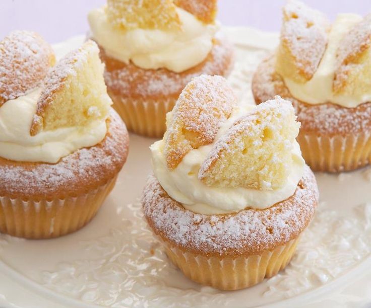 several cupcakes with icing and powdered sugar on top are sitting on a white plate