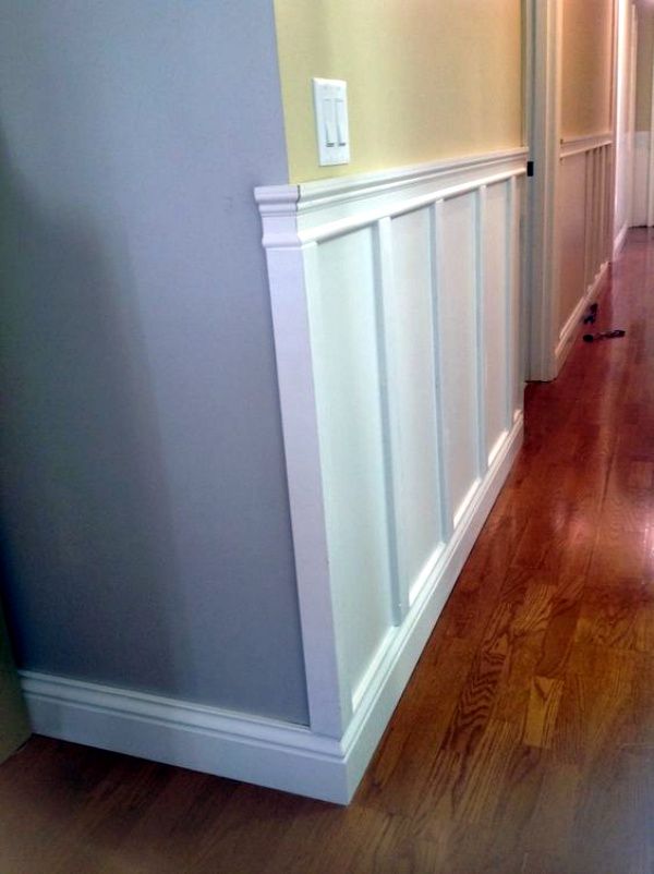 an empty hallway with hard wood flooring and white paneling on the side wall