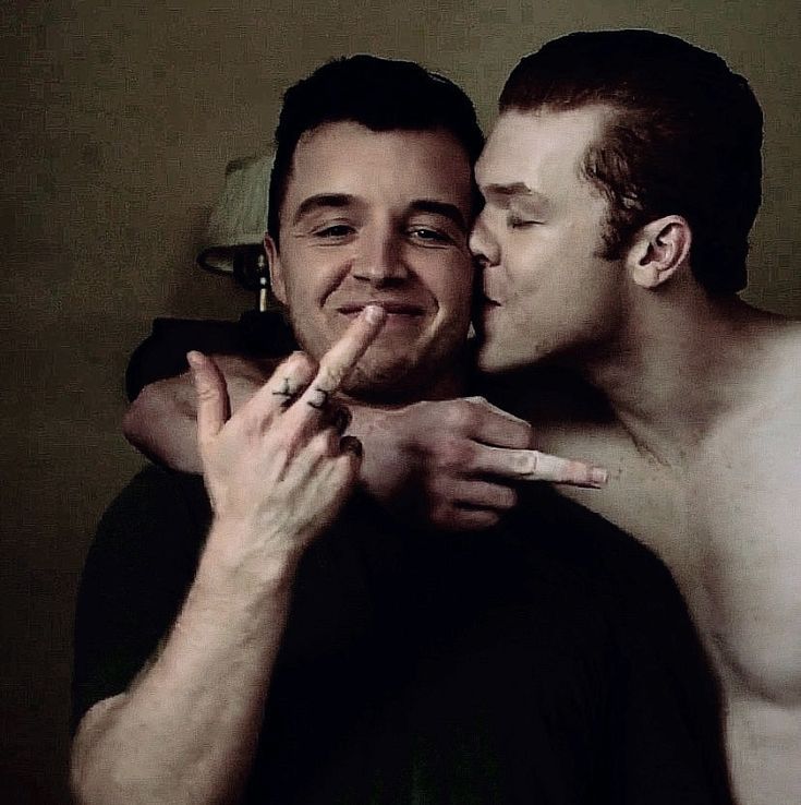 two shirtless men giving each other a kiss on the cheek with their fingers together