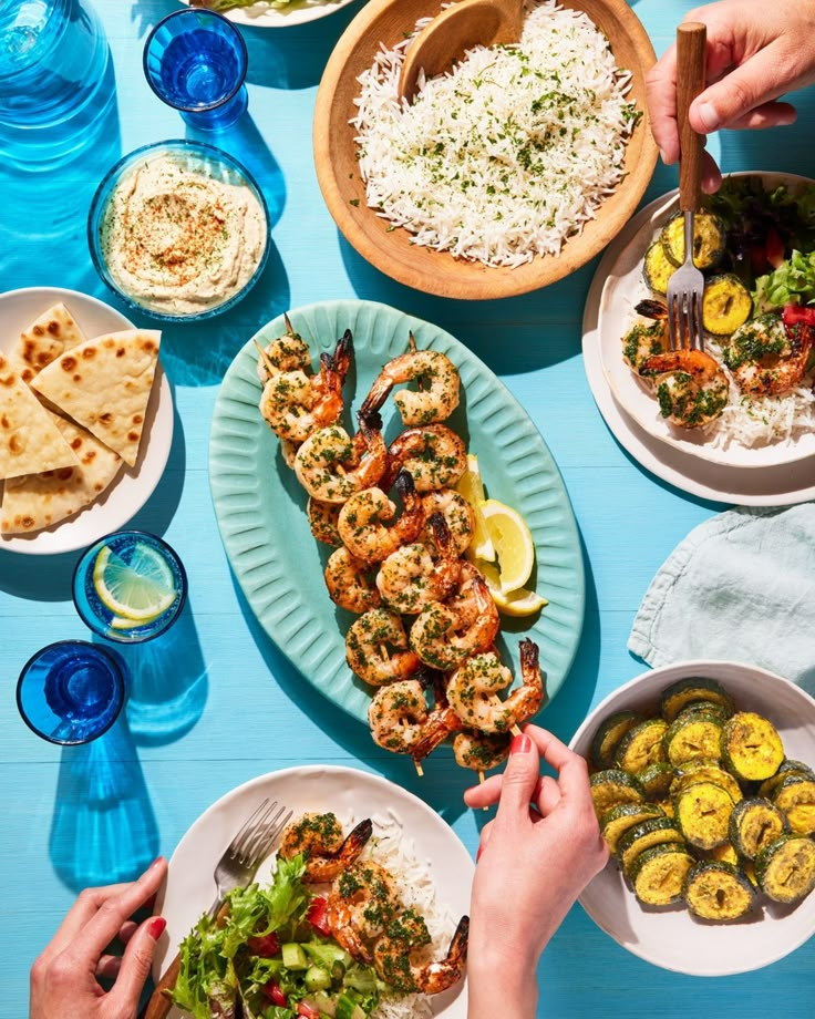 several plates of food on a blue table with people eating and serving them to each other