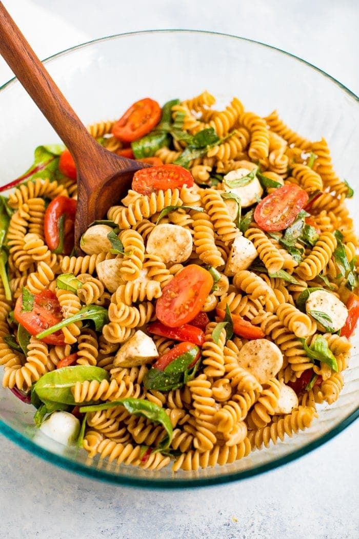 pasta salad with tomatoes, mozzarella and spinach in a glass serving bowl