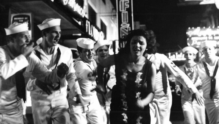 black and white photograph of people dancing on the street in front of a storefront