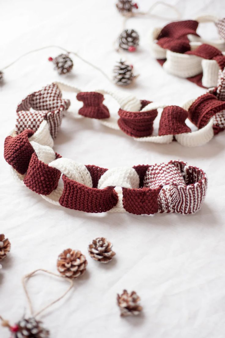 knitted christmas wreaths and pine cones on a white tablecloth with twine