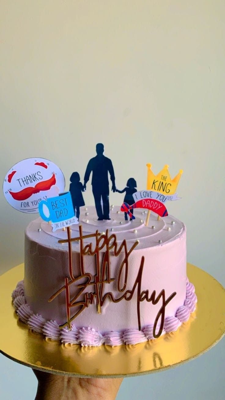 a hand holding a cake with the words happy birthday written on it and two people standing next to it