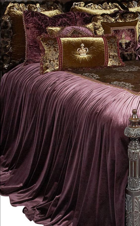 a bed with a purple bedspread and pillows on top of it, next to a night stand