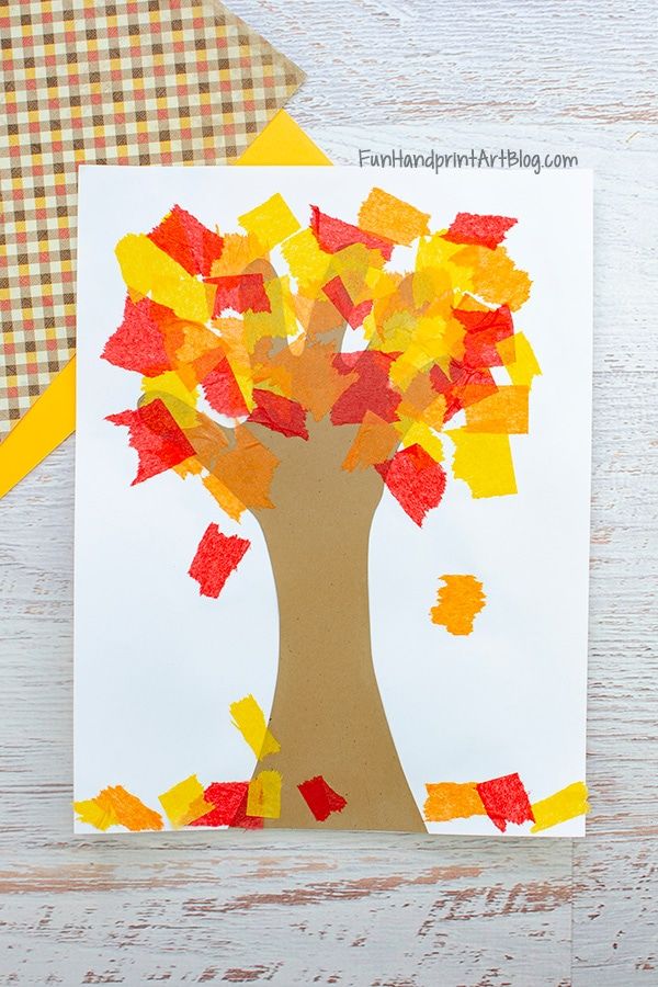 an autumn tree made out of tissue paper on a white wooden table next to a yellow and orange checkered napkin