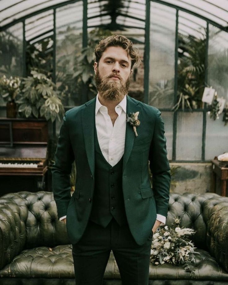 a man with a beard wearing a suit and bow tie standing in front of a couch