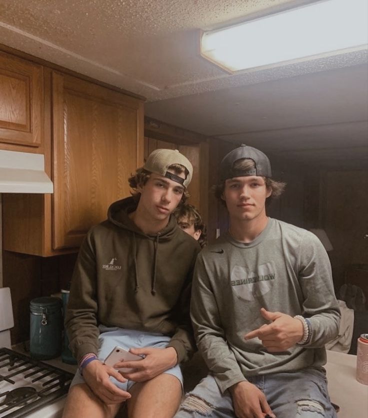 two young men sitting next to each other on a kitchen counter in front of a stove