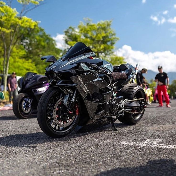 two motorcycles are parked on the side of the road as people stand around in the background