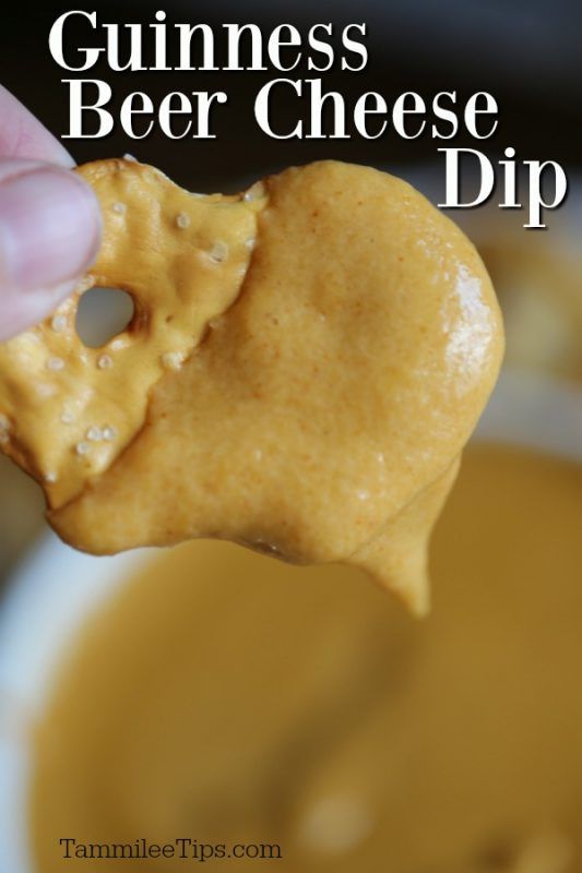 a hand holding up a piece of cheese that is dipped in peanut butter with the words guinness beer cheese dip on it