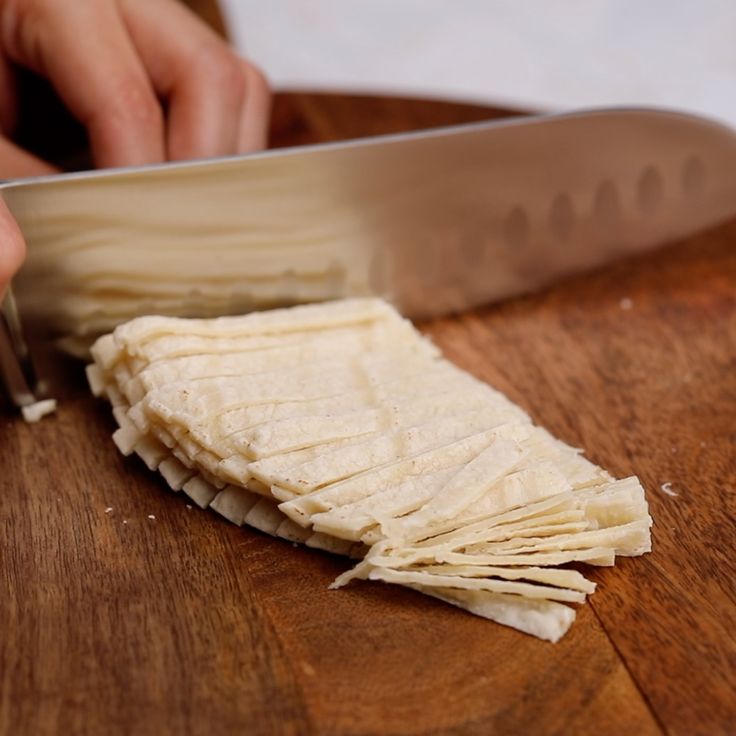 a person cutting up food on top of a wooden table next to a large knife