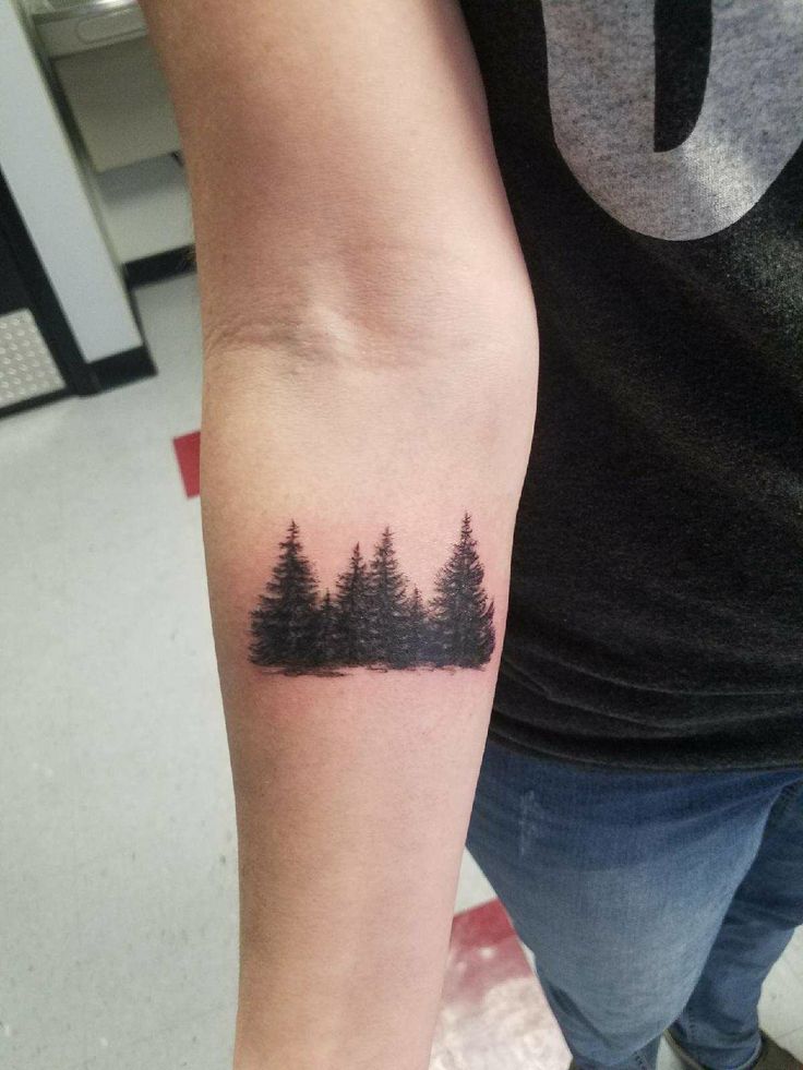 a person with a small tattoo on their arm that has trees in the middle of it