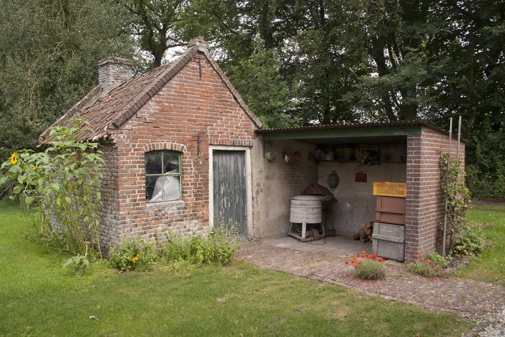 a small brick building sitting in the middle of a lush green field next to trees