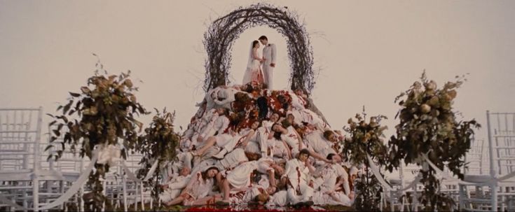 two people standing on top of a wedding dress made out of fake flowers and vines