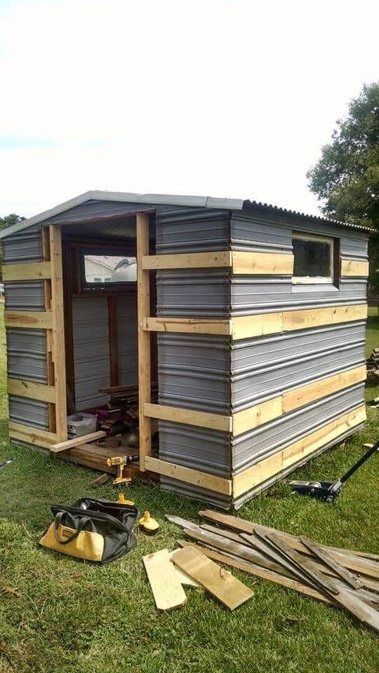 a small shed sitting on top of a lush green field next to a pile of wood