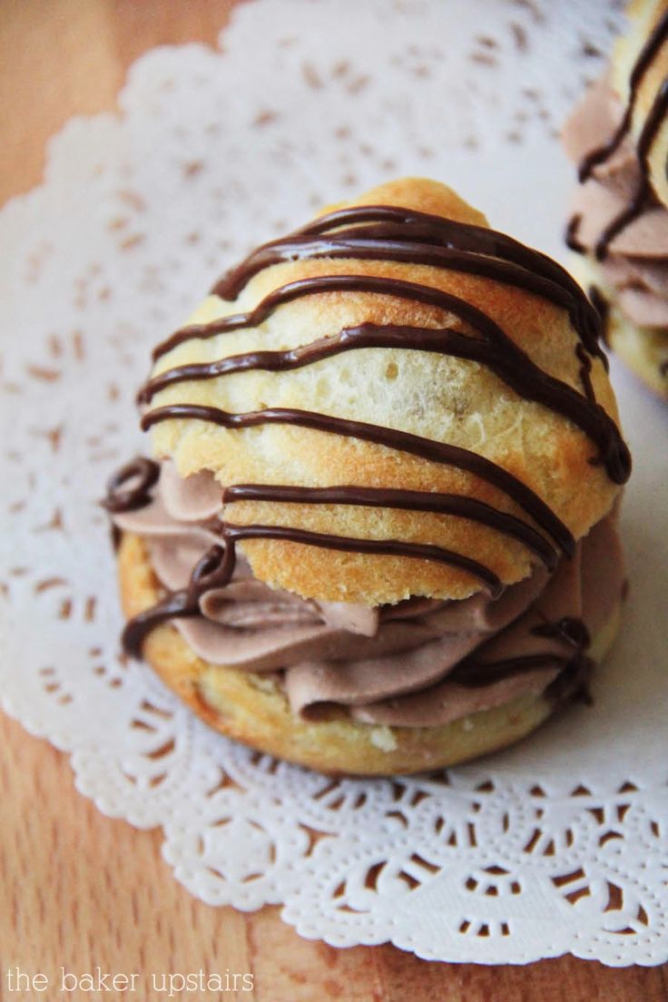 two chocolate covered donuts sitting on top of a doily