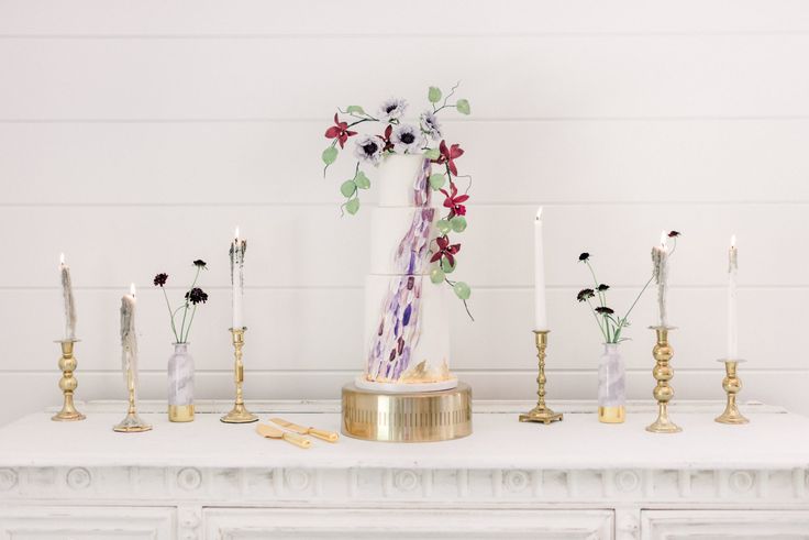 an arrangement of flowers and candles on a mantle in front of a white painted wall