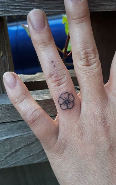 a person's hand with a small flower tattoo on their left thumb and finger