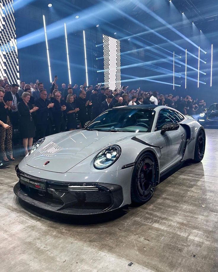 the porsche 912 gtr is on display at an event with people standing around