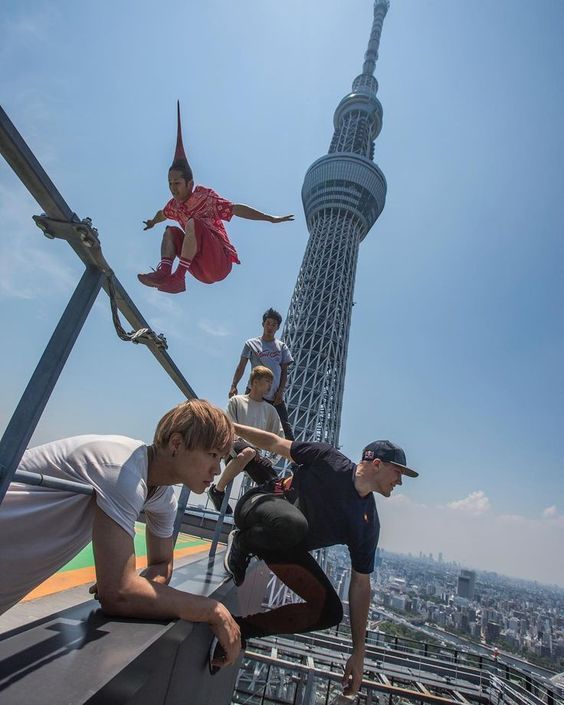 some people are standing on the edge of a building and one person is jumping in the air