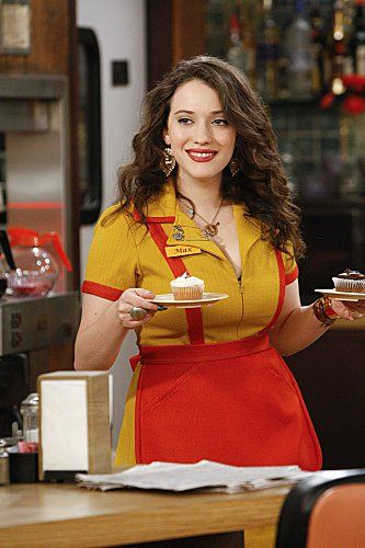 a woman in an orange and yellow dress holding a plate with cupcakes on it