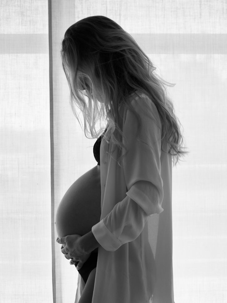 a pregnant woman standing in front of a window with her belly tucked under her shirt