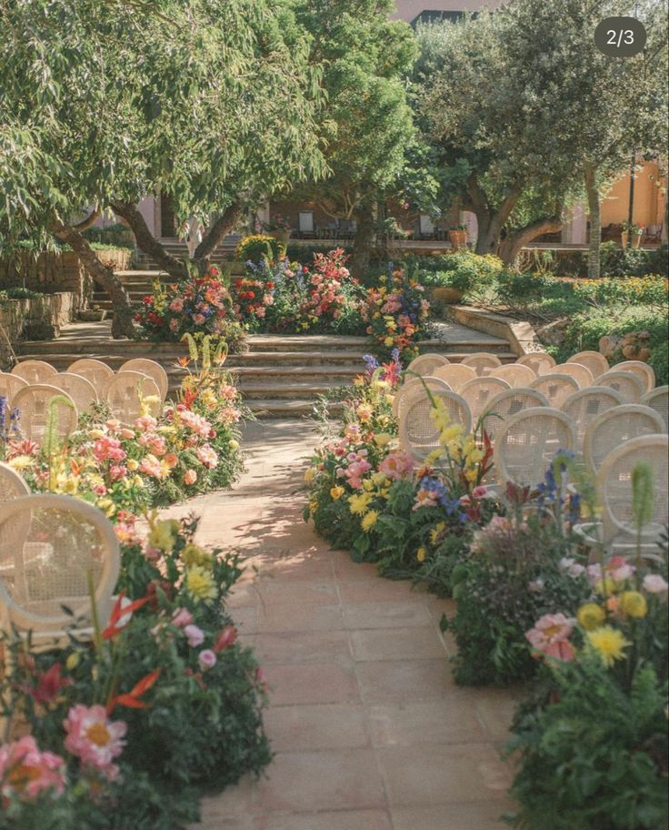 rows of chairs are lined up in the middle of an outdoor garden with flowers and greenery