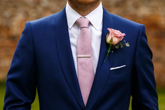 a man in a blue suit with a pink tie and rose boutonniere