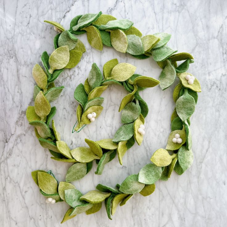 a wreath made out of green leaves and white flowers on a marble surface with pearls in the center