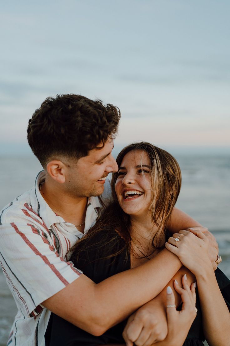 a man and woman hugging each other on the beach at sunset with the ocean in the background