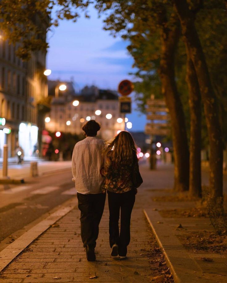 a man and woman walking down the street at night with their back to each other