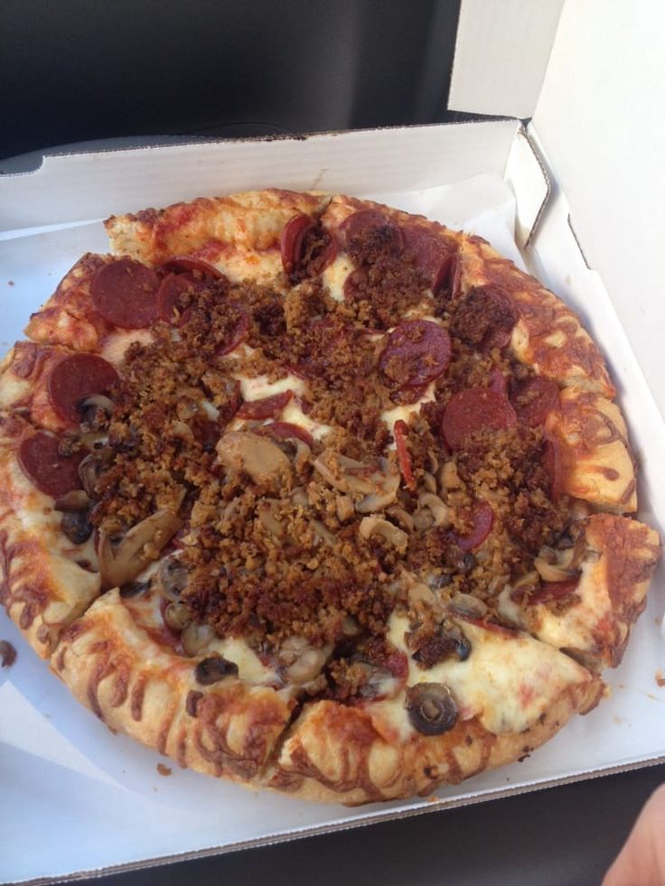 a pizza in a box with toppings on it sitting on a table next to a person's hand