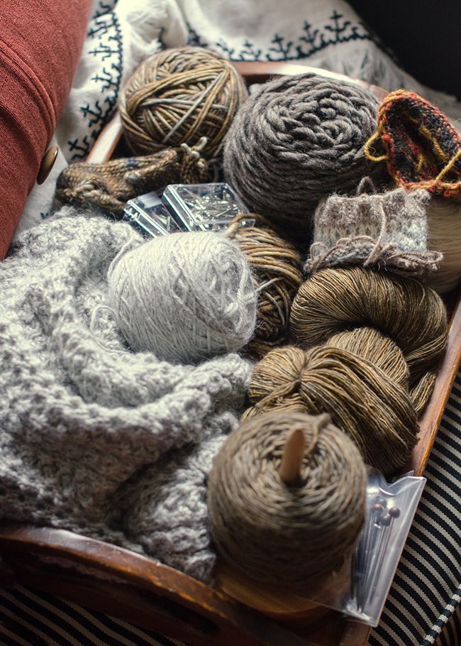 yarn and knitting needles in a basket on top of a bed next to a pillow