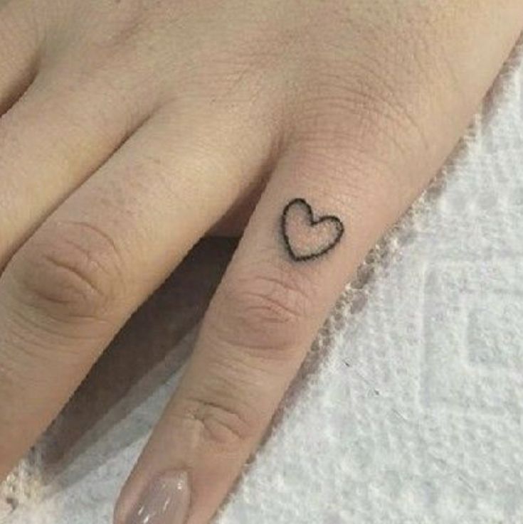 a woman's hand with a small heart tattoo on her left thumb and ring finger