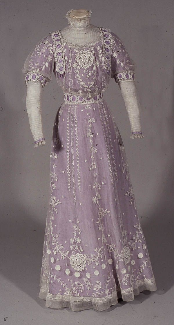 an old purple dress with white lace on the neck and sleeves, is displayed in front of a gray background