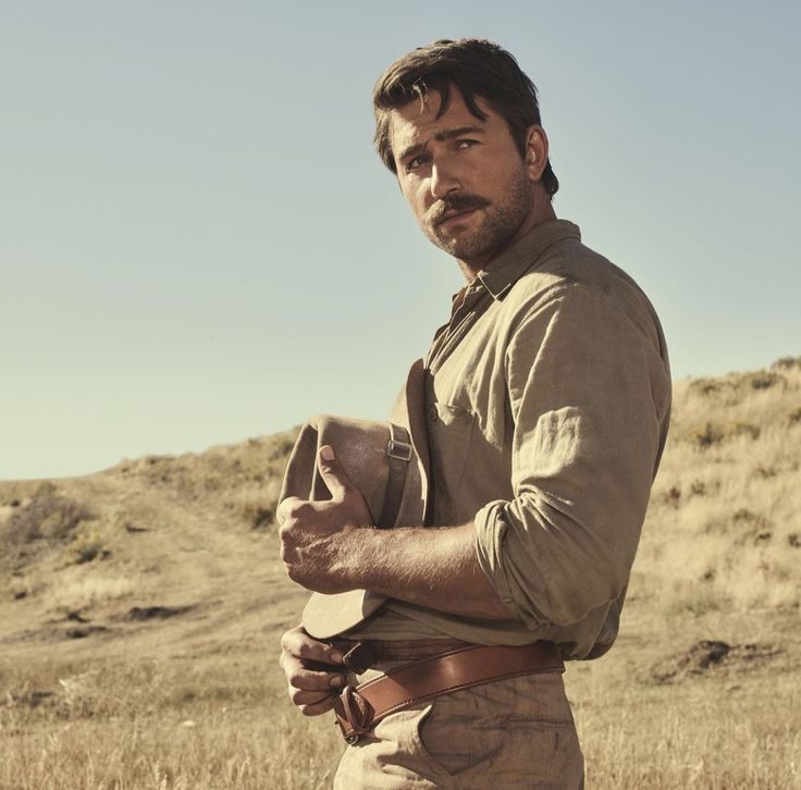 a man standing in a field holding a hat