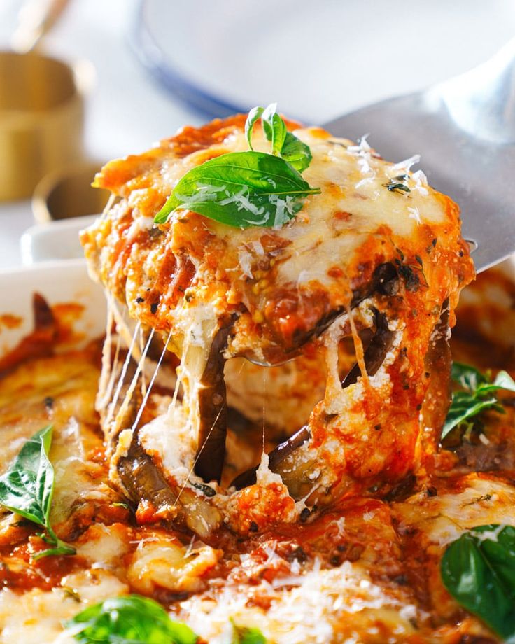 a piece of lasagna being lifted from a white dish with basil on top