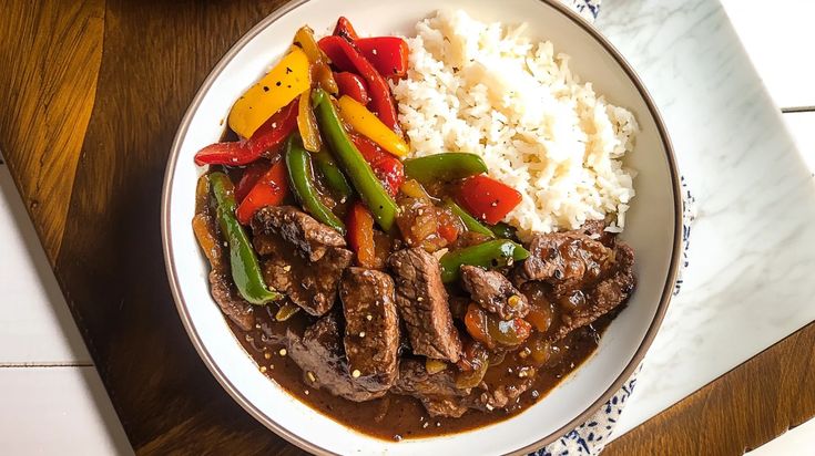 a white plate topped with meat and veggies next to rice on top of a wooden table