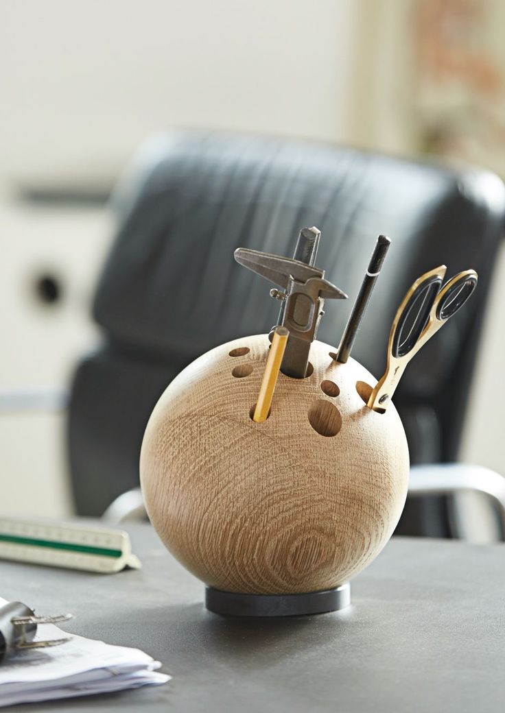 a wooden holder with scissors and other office supplies in it on a table next to a chair