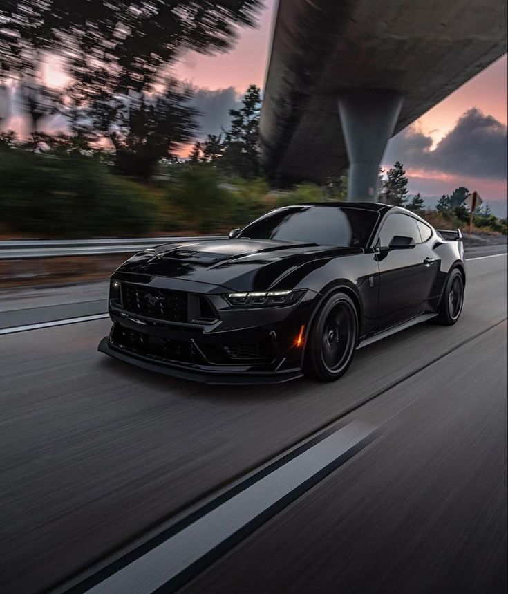 a black sports car driving down the road under a bridge at sunset or dawn with its lights on