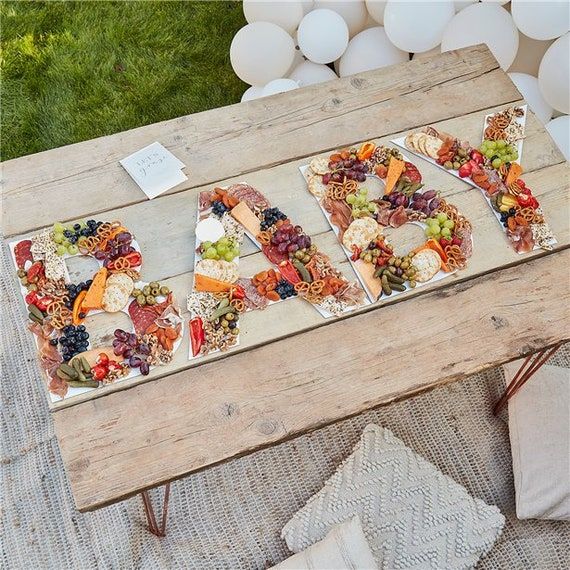 a wooden table topped with lots of different types of food next to white balloons in the background