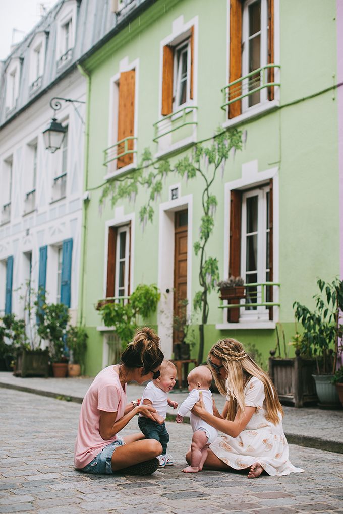 three people sitting on the ground in front of a green building with two babys