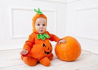 a baby dressed as a pumpkin sitting on the floor next to two large pumpkins